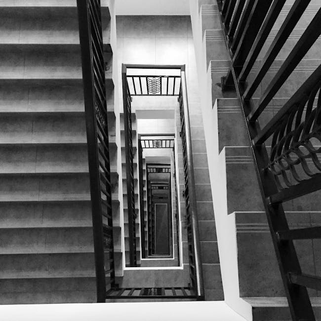 An interior view of a spiral staircase inside a residential property, featuring black metal railings and wooden steps. The staircase curves upwards, leading to an upper floor that is partially visible